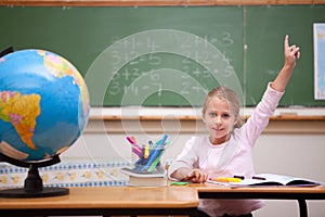 Cute schoolgirl raising her hand to answer a question