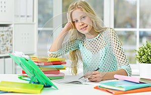 Cute schoolgirl sitting at desk and studying at home