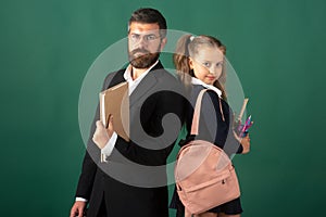 Cute schoolgirl with teacher in school. Studio portrait of tutor and young school girl with backpack and textbook on