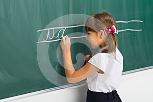 Cute schoolgirl writing on blackboard