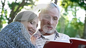 Cute senior couple viewing photoalbum, remembering funny moments of life