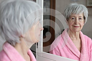 Cute senior woman looking at her reflection in the bathroom