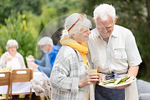 Cute seniors standing close to each other and hlding plate full of food during garden party