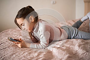 Cute serious girl lies with a mobile phone on the bed.close up side view photo