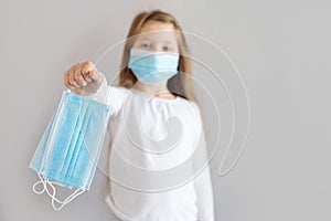 Cute serious girl with long blond hair in a mask, out of focus, holds medical masks on an outstretched arm. Virus protection.