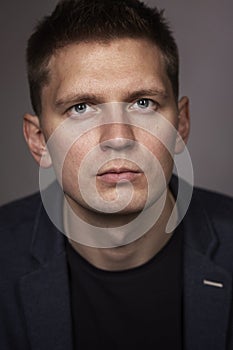 Cute serious young man in a jacket, close-up, gray background