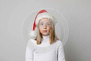 Cute shocked surprised child girl in Santa hat looking at camera on white background