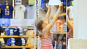 Cute shopaholic little child choose looking for clothes in clothing store.Cheerful baby shopper customer is looking and