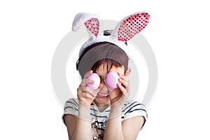 Cute short haired smiling little child wearing bunny ears on Easter day with two painted pink eggs in hands in front of face