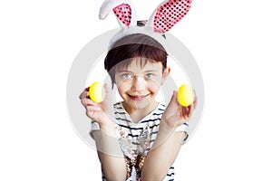 Cute short haired smiling little child wearing bunny ears on Easter day with two painted yellow eggs in hands isolated on white