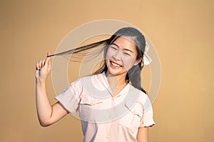 Cute Shy Asian Woman smile and play her hair in orange brown background at outdoor field in sunlight environment