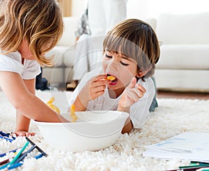 Cute sibling eating french fries on the floor