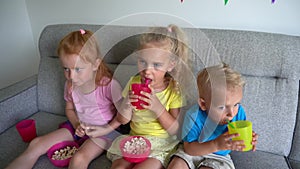 Cute siblings children eat popcorn drink juice and watch movie on home cinema