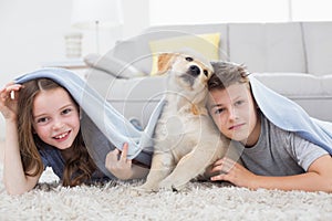 Cute siblings with dog under blanket in living room