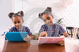 Cute siblings having the same hairstyles holding pink and blue tablets
