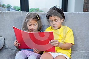 Cute siblings reading a book on the sofa