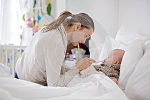 Cute sick child, baby boy, staying in bed, mom giving him medici