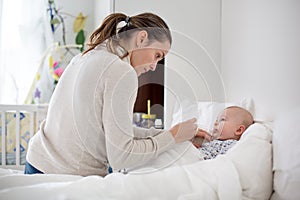 Cute sick child, baby boy, staying in bed, mom giving him medici