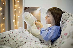 Cute sick child, boy, staying in bed, playing with teddy bear