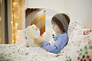 Cute sick child, boy, staying in bed, playing with teddy bear