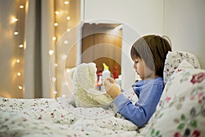 Cute sick child, boy, staying in bed, playing with teddy bear