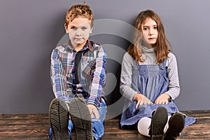 Cute sister and brother sitting near wall.