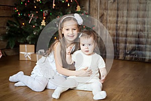 Cute sisters in front of decorated Christmas tree