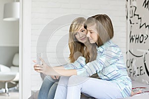 Cute sisters photographing themselves through cell phone at home