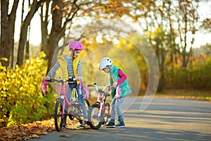 Cute sisters riding bikes in a city park on sunny autumn day. Active family leisure with kids. Children wearing safety hemet while