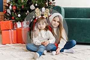 Cute sisters are sitting in the Christmas interior and celebrating Christmas and New Year.