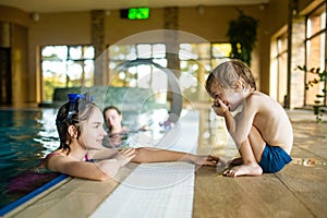 Cute sisters and a toddler having fun in indoor pool. Children learning to swim. Kids having fun with water toys. Family fun in a