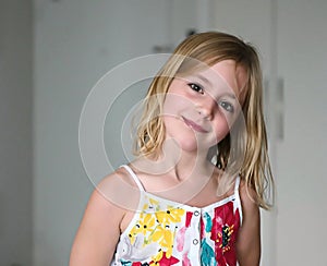 Six year old blonde girl in a summer white dress with flowers smiling on an abstract background