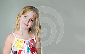 Six year old blonde girl in a summer white dress with flowers smiling on an abstract background