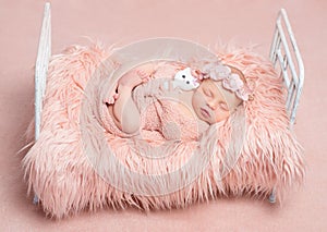 Cute sleeping newborn girl with toy cat on little bed