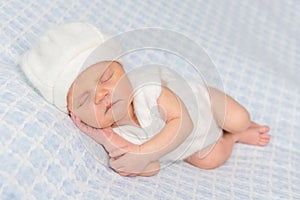 Cute sleeping newborn in white romper and hat