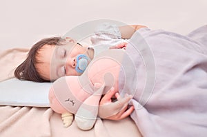 Cute sleepy Asian infant girl sleeping on soft bedding with pacifier, Little kid taking a nap in bed while hugging soft plush