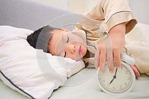 Cute sleepy little kid lying on the bed and stopping, turn off alarm clock in the bedroom at home