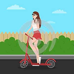 Cute slender young girl in glasses, a T-shirt and a skirt coquettishly touches brown hair. Standing by the scooter holding the
