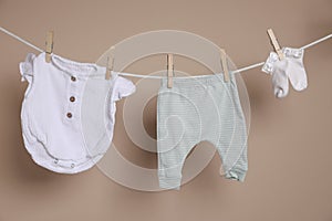 Cute small baby clothes hanging on washing line against brown background
