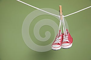 Cute small baby shoes hanging on washing line against green background, space for text