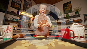 Cute small boy in Gingerbread apron placing cookies on baking tray cozy kitchen