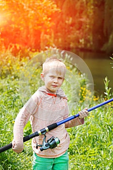 Cute small boy stand near a river with a fishing rod in his hands.