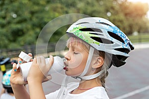 Cute small caucasian girl kid in safety sport helmet drinking fresh water from bottle after exercise bike, scooter or