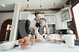 Cute small child daughter helping mum kneading preparing dough in bowl together in modern kitchen