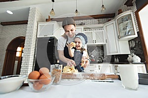 Cute small child daughter helping mum kneading preparing dough in bowl together in modern kitchen