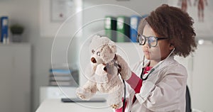 Cute small child pretending to be doctor examining teddy bear with stethoscope
