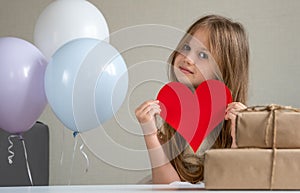 Cute small girl holding big red heart near air balloons and gifts. Valentines Day, love, mothers fathers Day, romantic