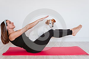 Cute small jack russell dog doing yoga on a mat at home with her owner. Healthy lifestyle indoors