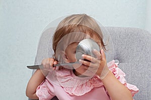 Cute small kid girl eats from big spoon. hungry funny baby.