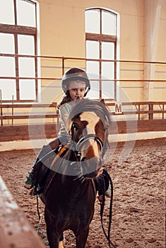 Cute small kid girl learning to ride a horse in farm corral